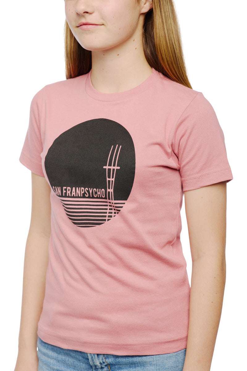 The person is sporting a pastel pink Youth Sutro Tower Tee, made from 100% cotton, showcasing a striking black circular graphic and text, paired perfectly with light blue jeans.