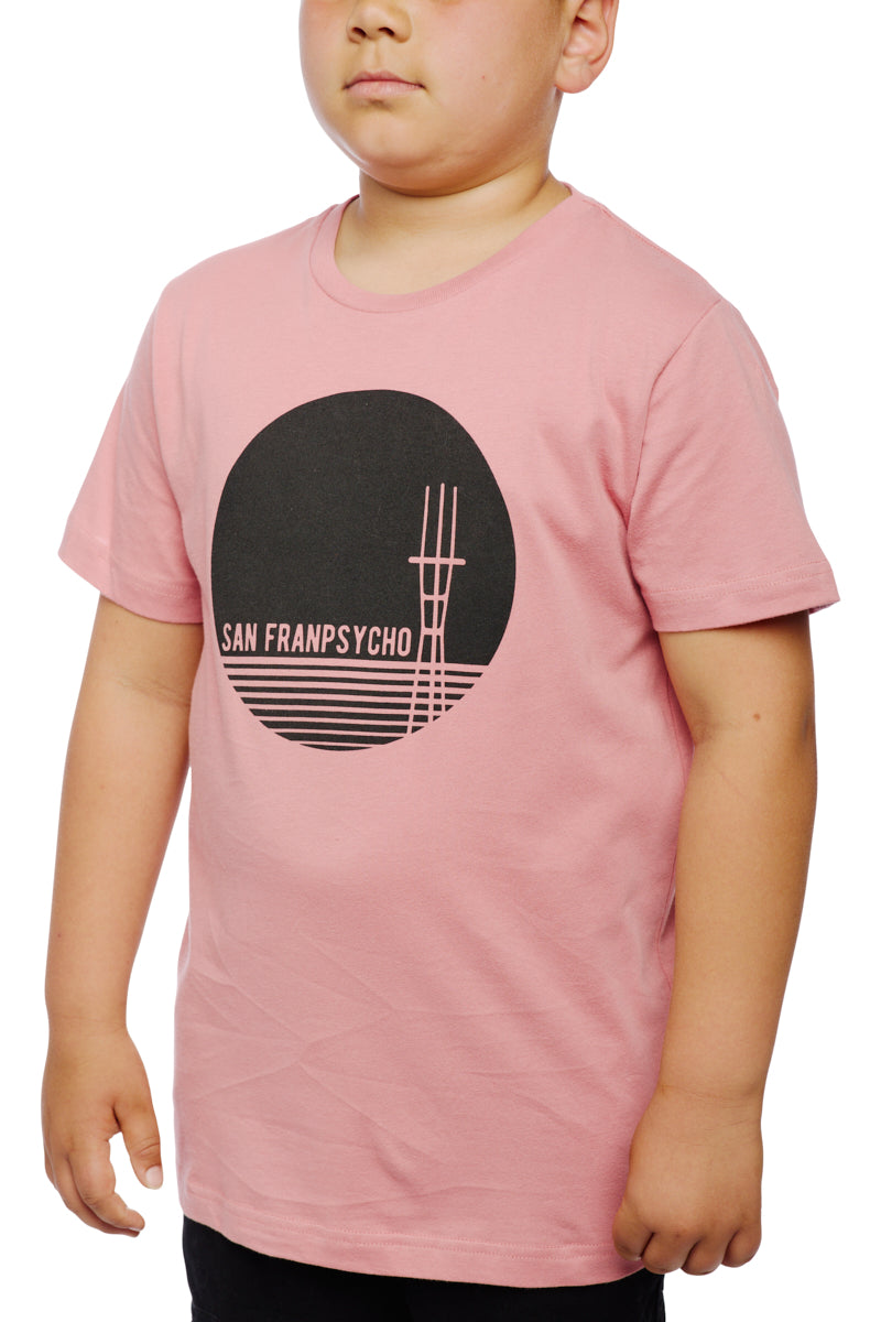 A child in a pastel pink Youth Sutro Tower Tee showcases a black circle design with bold SAN FRANPSYCHO text, made from 100% cotton for comfort.