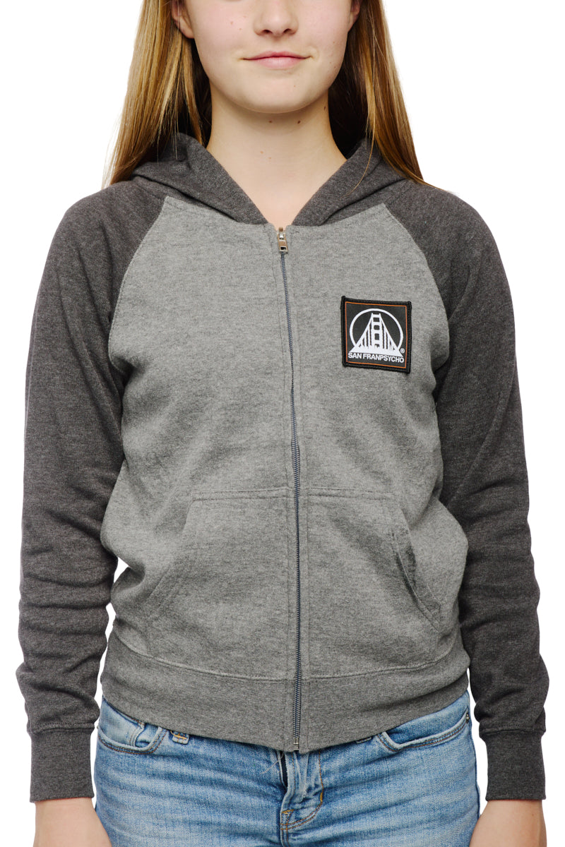 A person wearing the Youth Two Tone Patch Hoodie by San Franpsycho, featuring a gray and dark gray design with a chest logo, stands against a white background.