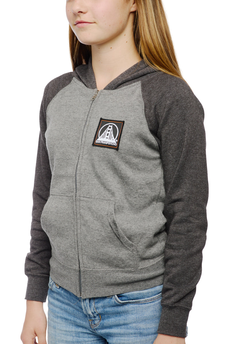 A young person sports the Youth Two Tone Patch Hoodie from San Franpsycho, featuring a gray body with dark sleeves and a front logo, effortlessly paired with blue jeans.