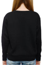 A person with long hair, wearing a hand-printed black Youth Outer Sunset Crewneck and blue jeans, is captured from behind while strolling through the Outer Sunset neighborhood of San Francisco.