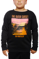 A child wears the Youth Outer Sunset Crewneck, a black sweatshirt adorned with a hand-printed, colorful sunset graphic and the text THE OUTER SUNSET SAN FRANPSYCHO, embodying the lively spirit of San Francisco.