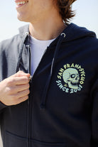 The Zebra Skull Zip-Up Hoodie from the Spring 2024 collection features a striking skull design and text, partially unzipped to reveal a white Zebra Skull Tee underneath.