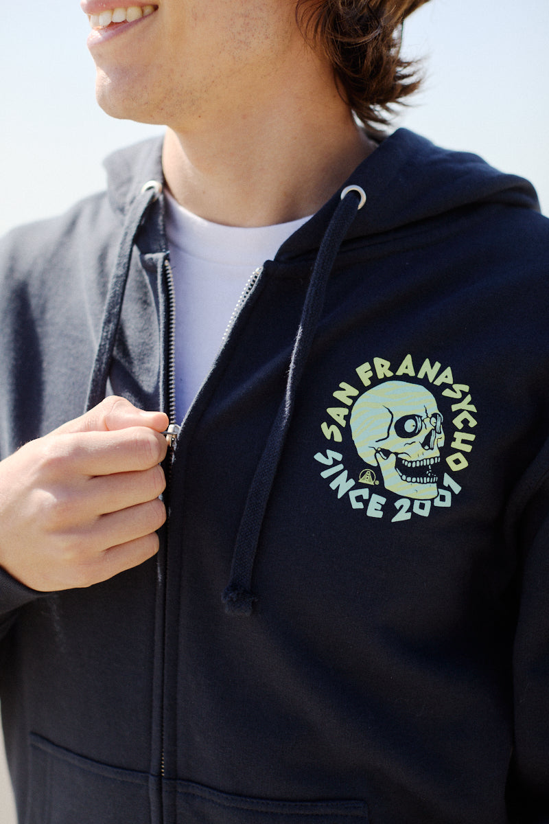 The Zebra Skull Zip-Up Hoodie from the Spring 2024 collection features a striking skull design and text, partially unzipped to reveal a white Zebra Skull Tee underneath.