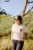 On a sunny day, a person in sunglasses and the Yin-Yang Tee - White stands outside, smiling with their hands in pockets, capturing an 80s-inspired vibe.