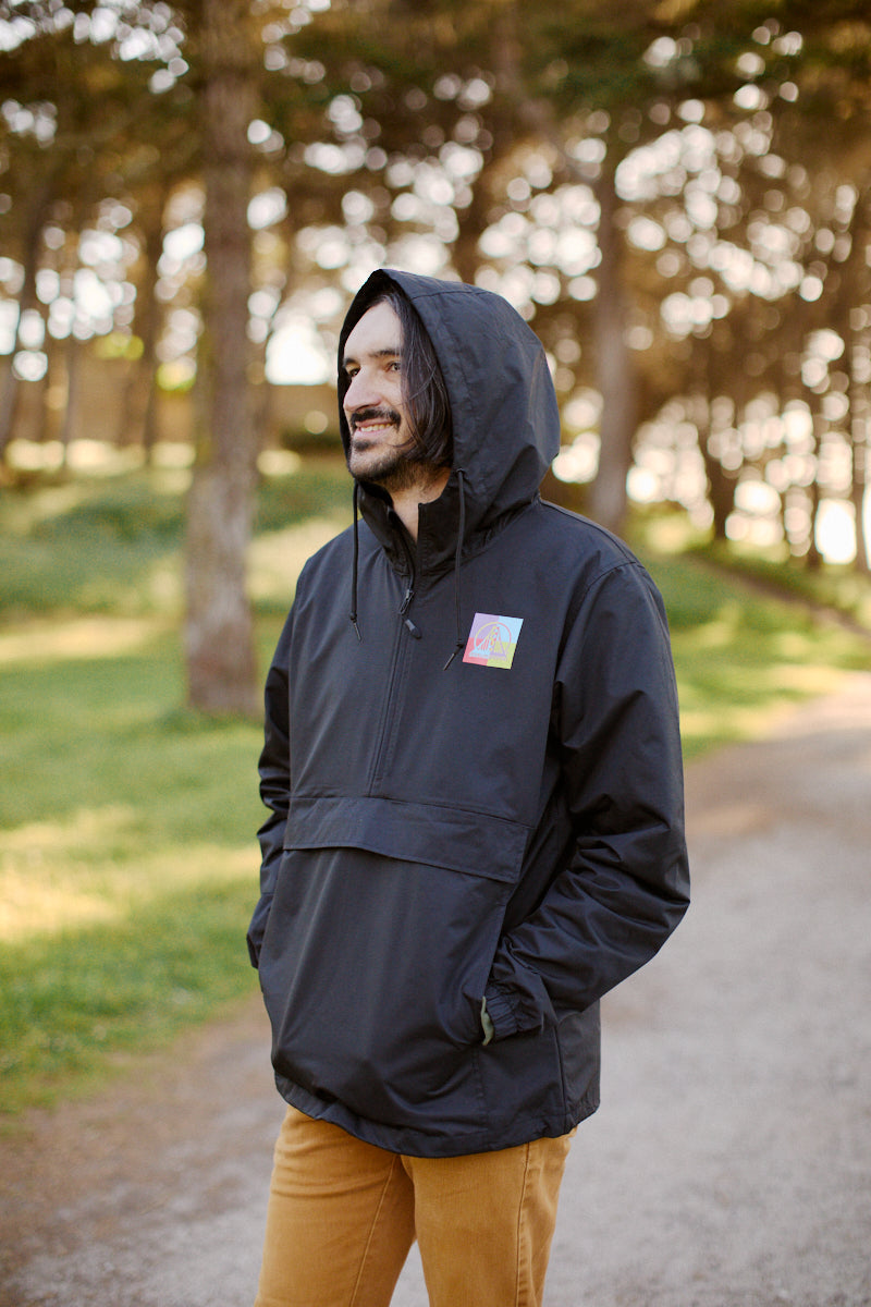 A man wearing a Colorblock Windbreaker and brown pants stands on a forest path, smiling.
