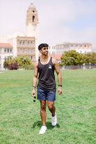 A man in a modern fit Acid Logo Tank Top and shorts strides across the grass, with towering buildings in the backdrop, showcasing both style and comfort.