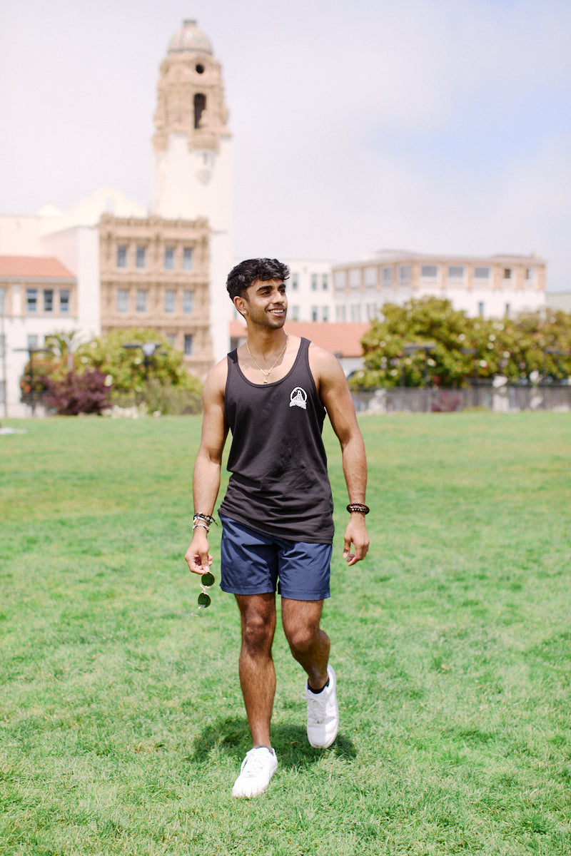 A man in a modern fit Acid Logo Tank Top and shorts strides across the grass, with towering buildings in the backdrop, showcasing both style and comfort.