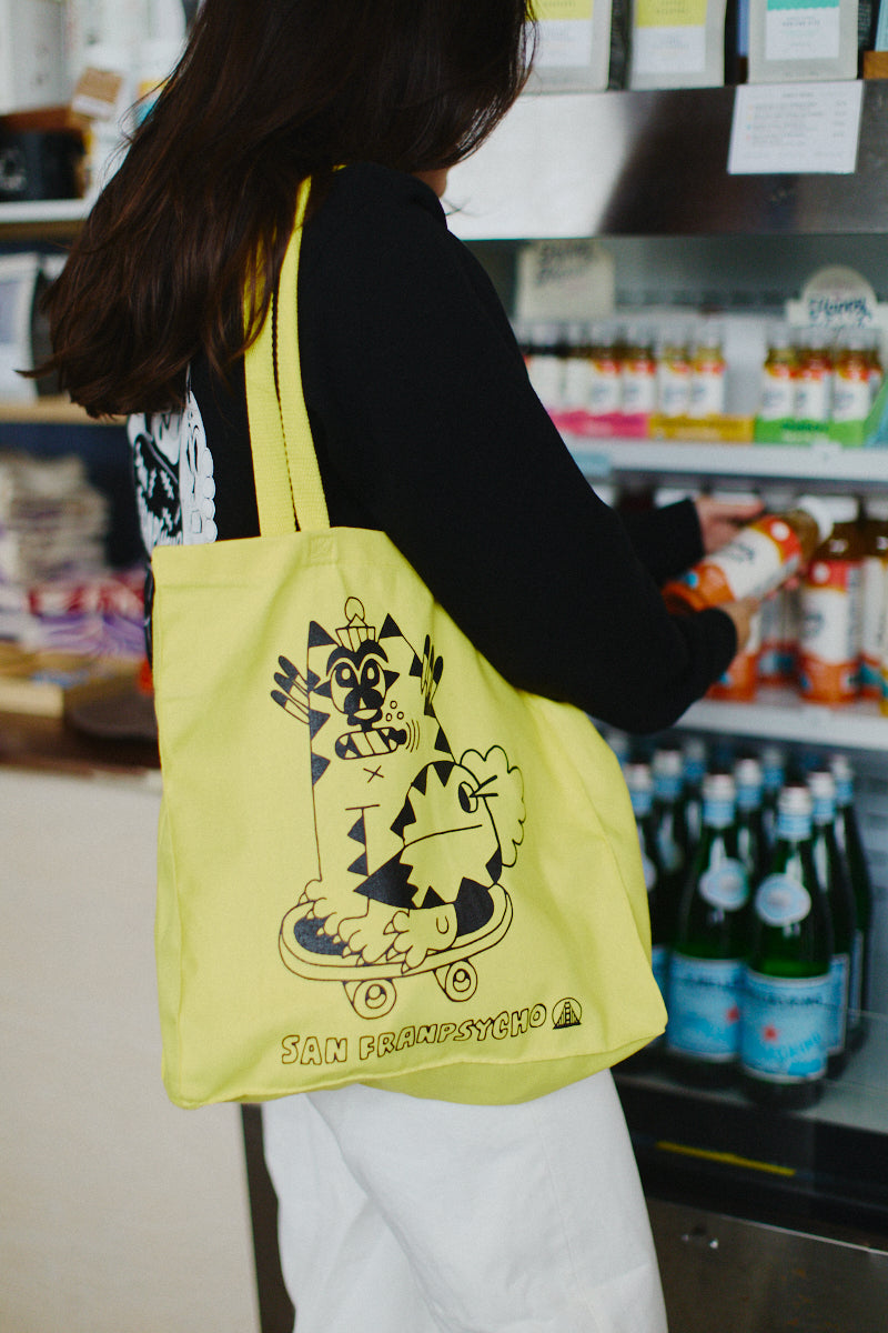 A person with a hand-printed yellow Kitty Poof Tote, crafted from 100% canvas, browses drinks in a store.