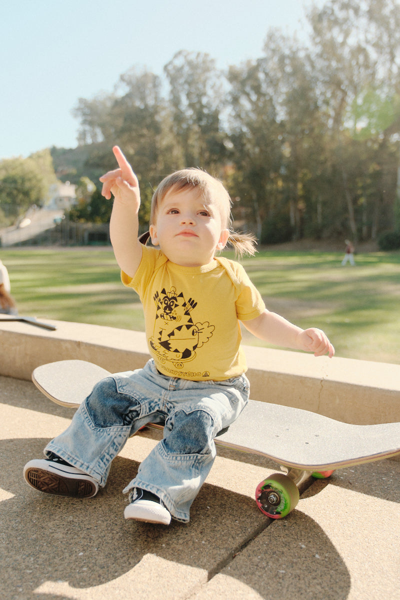 toddler sitting on skateboard wearing yellow Kitty Poof Onesie