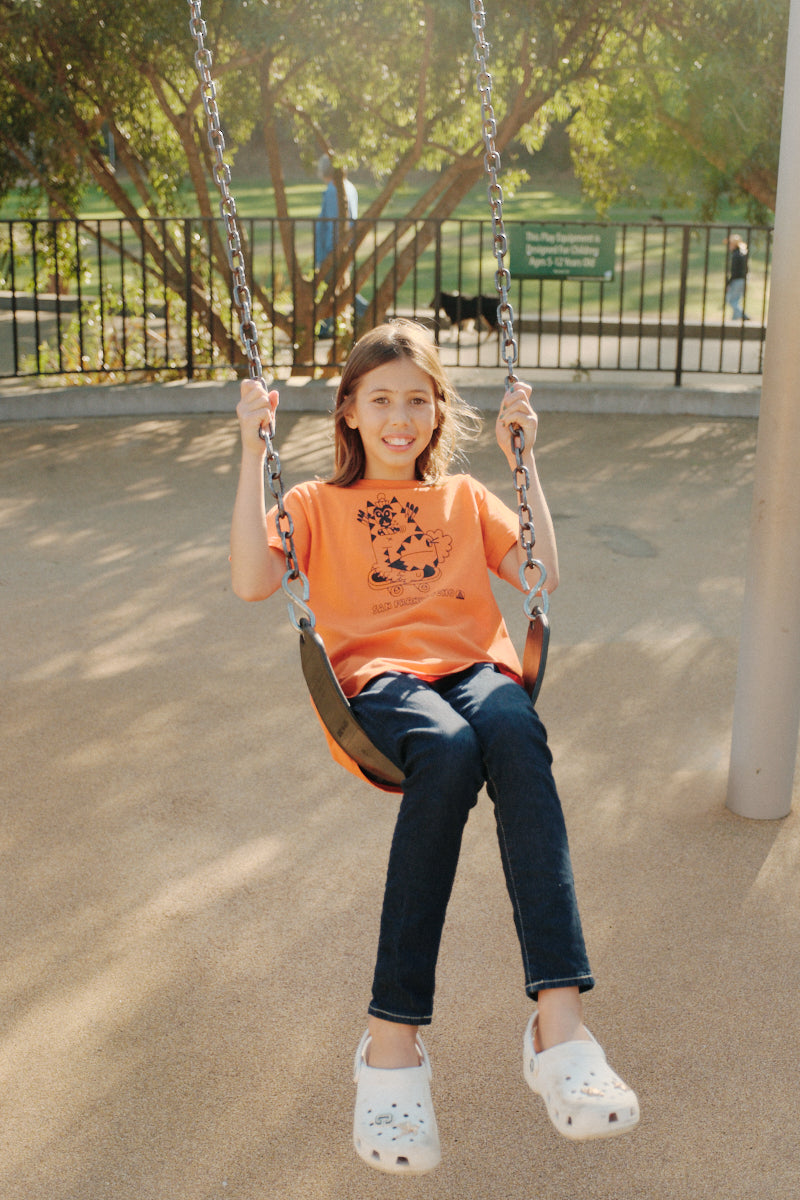girl riding on swingset wearing Youth Kitty Poof orange Tee