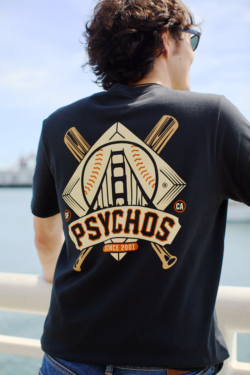 A man stands by the water in a hand-printed Psychos Logo Tee, displaying his black and orange pride with its distinct San Francisco baseball-themed design.