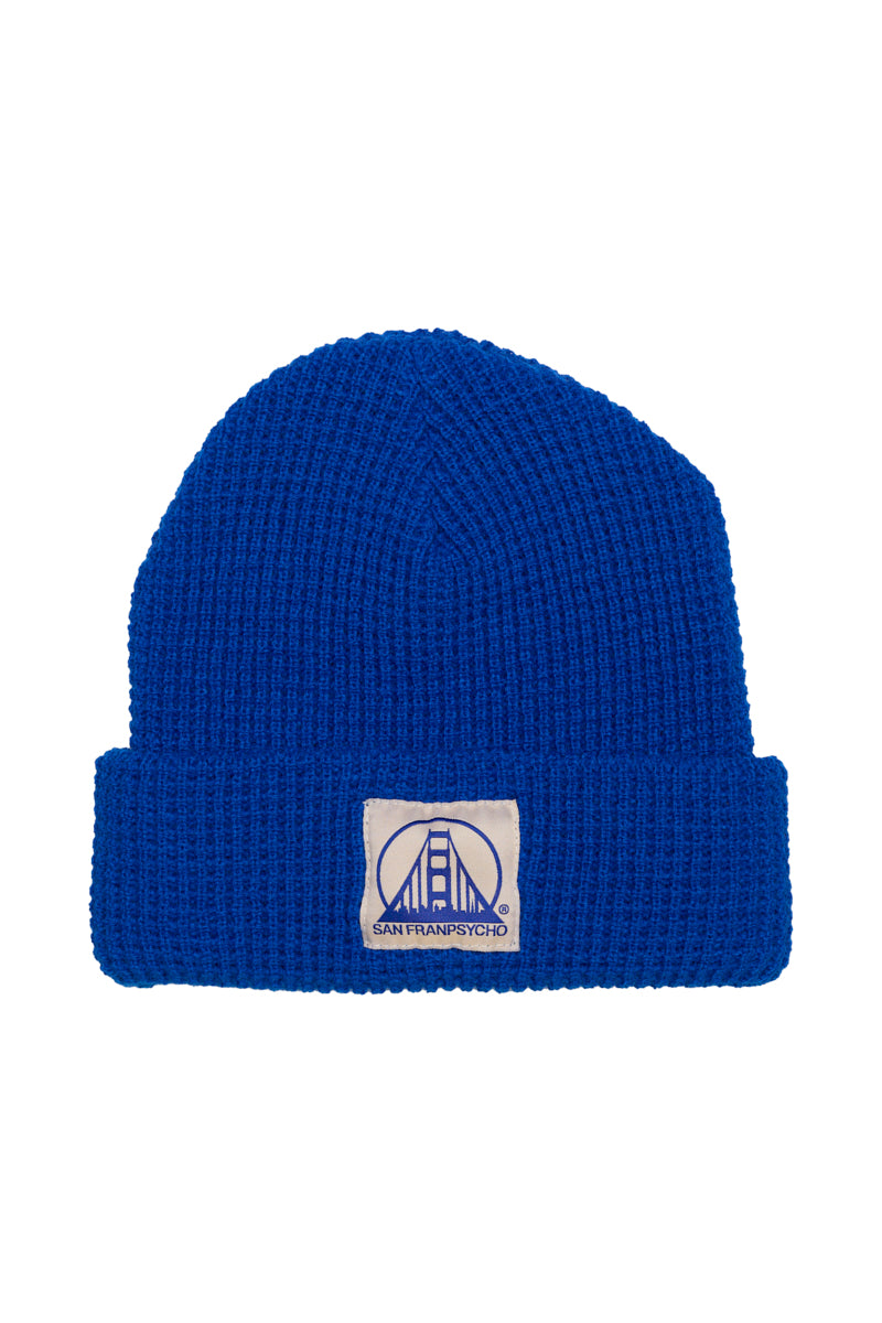 The Royal Blue Waffle Beanie w/ Natural/Blue Logo combines style with soft comfort, featuring a patch with a stylized bridge design.