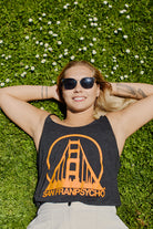 A woman relaxes on green grass, smiling in sunglasses and wearing the Women’s Logo Tank - Charcoal & Orange, featuring a relaxed fit from the basics line.