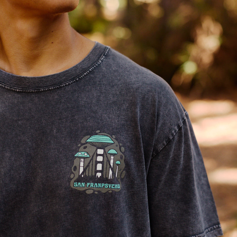 Young person outdoors wearing the Mind Bloom Tee, a mineral wash shirt with a UFO, subtle skull and mushroom graphics, and San Franpsycho text.