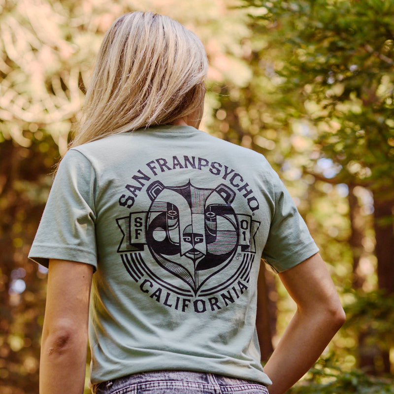A woman outdoors wears the Bear Essentials Tee, featuring the iconic California bear among green trees in San Francisco.