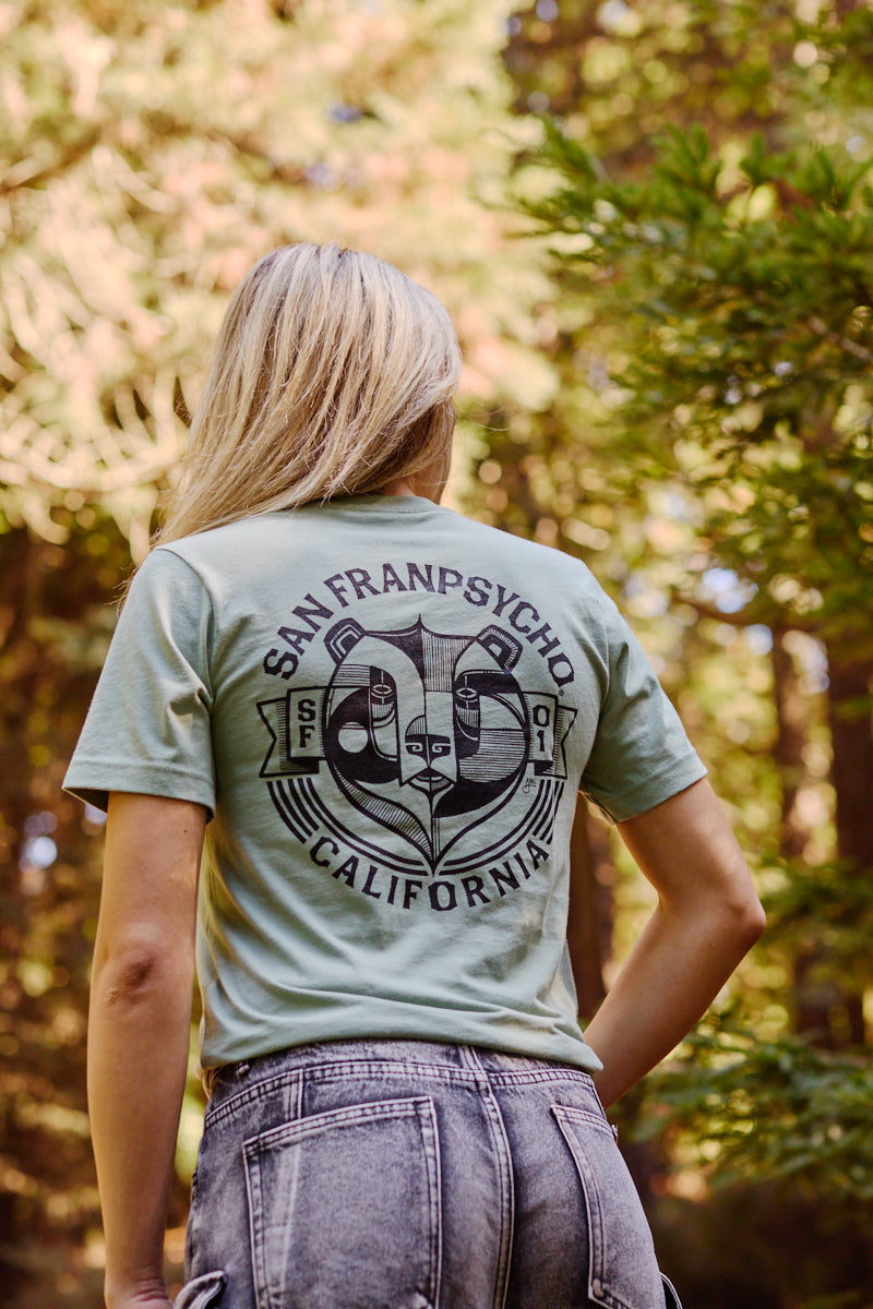 A woman outdoors wears the Bear Essentials Tee, featuring the iconic California bear among green trees in San Francisco.
