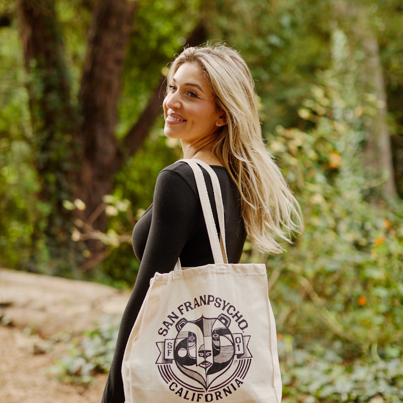 A woman outdoors smiles while carrying the Bear Essentials Tote, a San Franpsycho California canvas bag featuring a graphic logo.