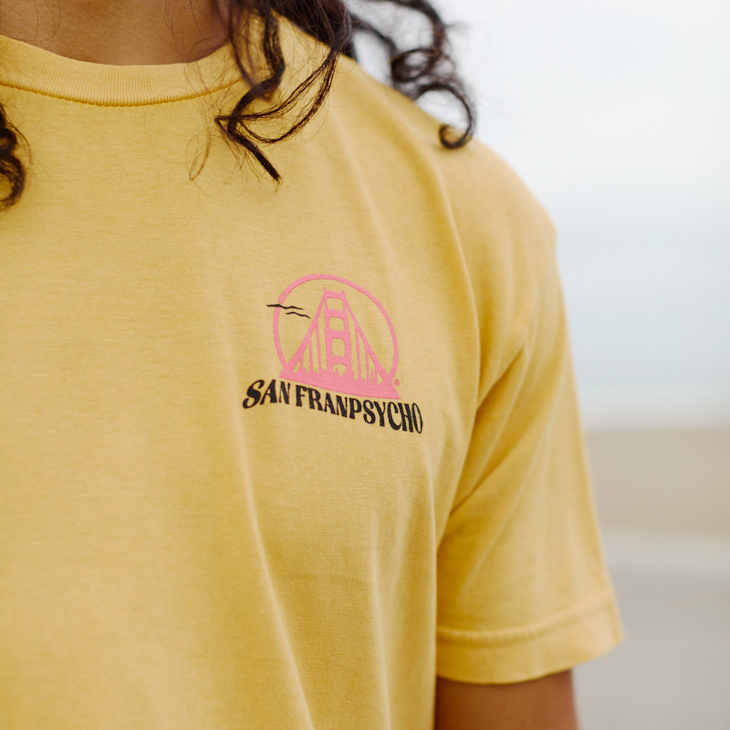 Wearing the Kelly's Cove Tee—a yellow shirt with a pink Golden Gate Bridge and San Franpsycho logo on the chest—is perfect for channeling iconic coastal vibes in classic San Francisco style.