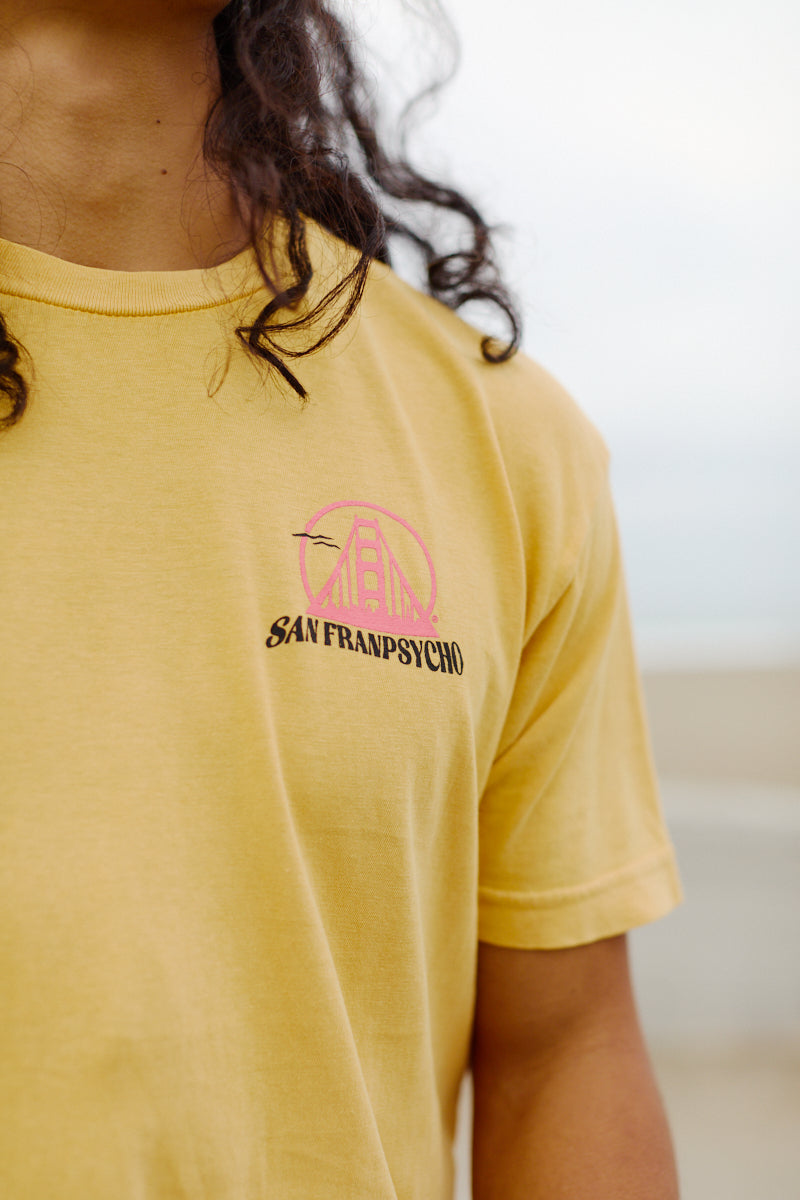 Wearing the Kelly's Cove Tee—a yellow shirt with a pink Golden Gate Bridge and San Franpsycho logo on the chest—is perfect for channeling iconic coastal vibes in classic San Francisco style.