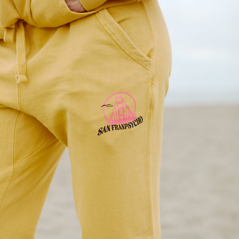 Someone wearing Kelly's Cove Joggers in yellow with a pink and black San Franpsycho logo, standing on the sandy beach.