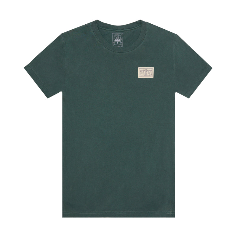 The Bridge Co Tee is a dark green heavyweight cotton shirt with a small rectangular logo patch on the left chest, ideal for a workwear-inspired style.