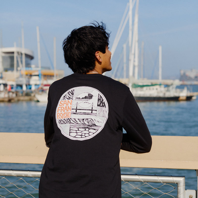 Wearing an Elemental Long Sleeve, a person leans on a waterfront railing with boats and a marina in the background.
