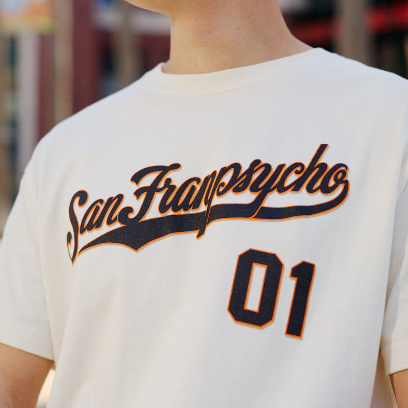 Person smiling, wearing a hand-printed Psychos Script Tee - Natural by San Franspycho 01, with black and orange details that pop and visible arm tattoos.