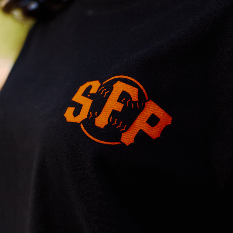 Close-up of the Black & Orange Psychos Tee—a black shirt featuring bold black and orange accents, the SCP logo, and a baseball graphic in the background.
