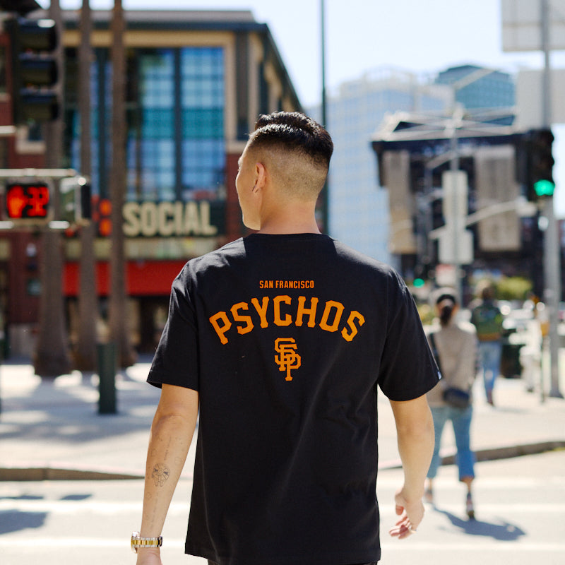 A man crosses a city street sporting the Black & Orange Psychos Tee, showing off his black and orange pride.
