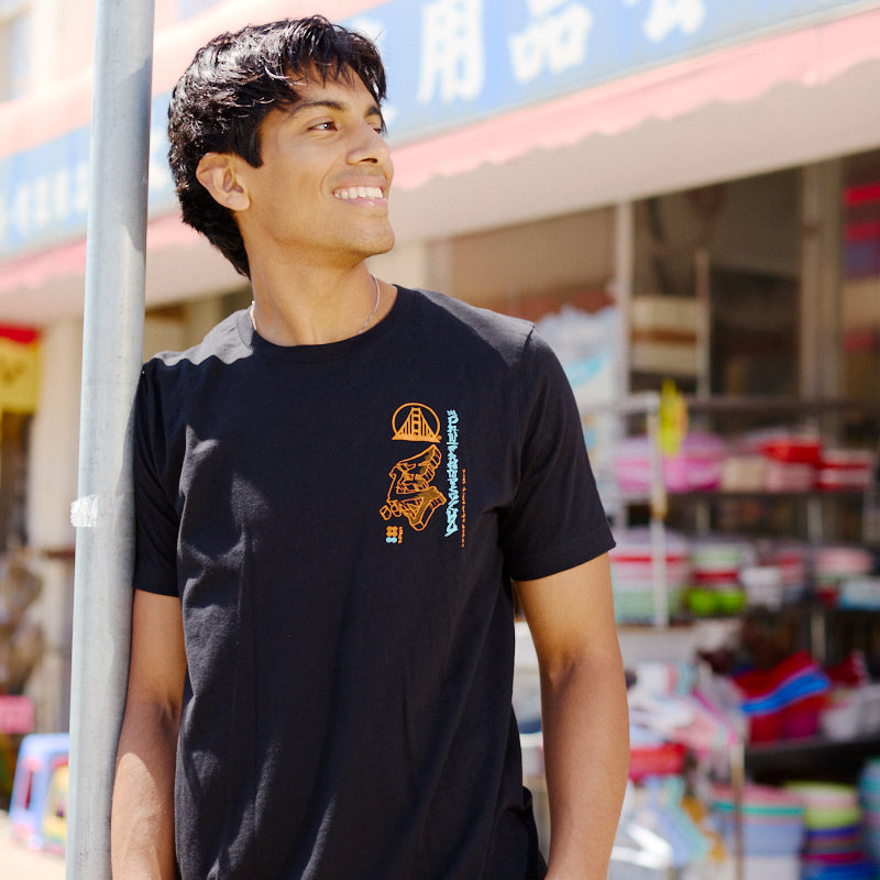 A smiling young man wearing the Year of the Horse Tee stands outside a store with colorful items and Chinese signage, celebrating Lunar New Year.