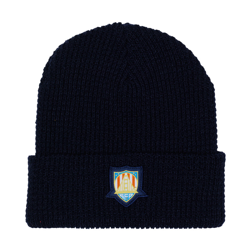 The WC x SFP Beanie is a black knit hat featuring a colorful embroidered shield logo on the folded brim, inspired by the US Men's National Team.