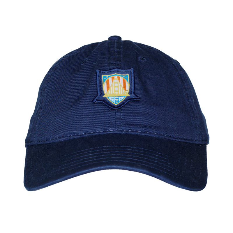 Support the US Men's National Team with the WC x SFP Patched Hat—navy blue baseball cap with a vibrant embroidered shield logo, perfect for cheering during the World Cup. Shown on a white background.