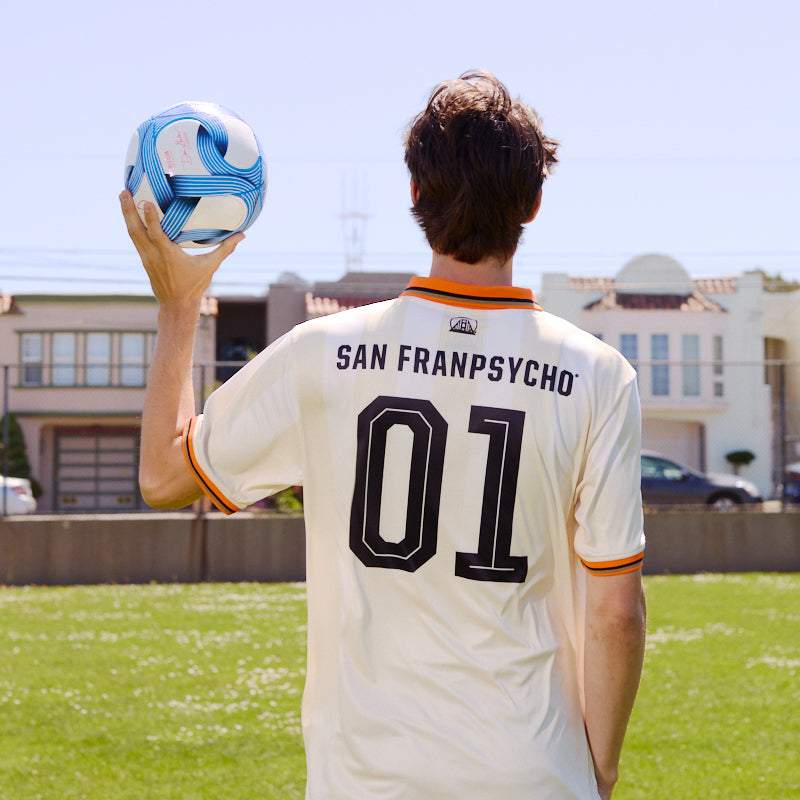 Person holding a blue and white soccer ball, wearing the WC x SFP Jersey - Away inspired by the US Men's National Team, standing on grass.