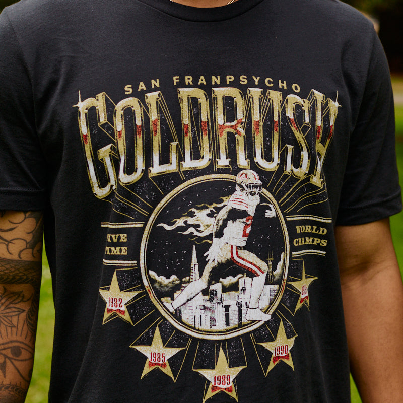 A man wearing the Gold Rush Tee - Vintage Black, featuring a football graphic and championship years, celebrates the spirit of San Francisco.