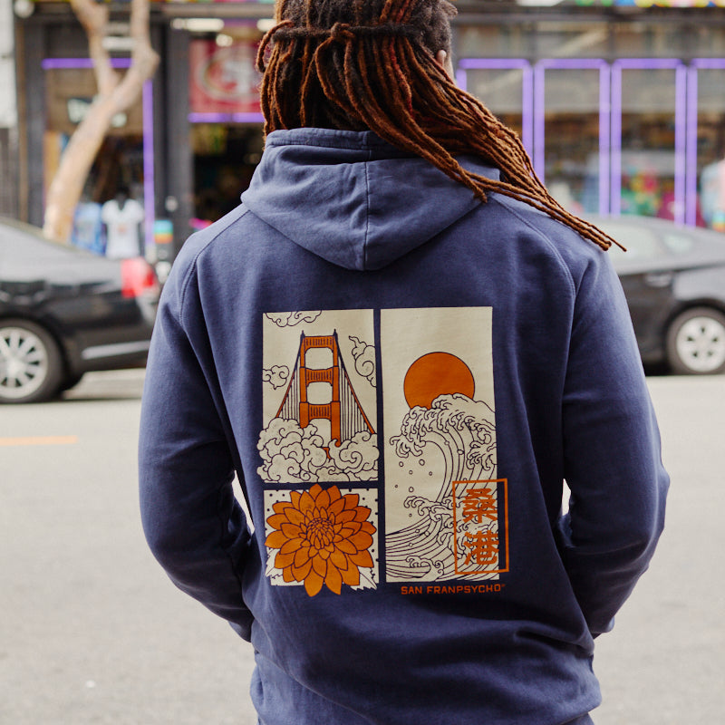 A person with dreadlocks wears the Sunset Dahlia Pullover Hoodie, a vintage mineral wash hoodie adorned with Japanese art-inspired graphics of the Golden Gate Bridge, waves, sun, and a flower—echoing the design found on the Sunset Dahlia Tee.