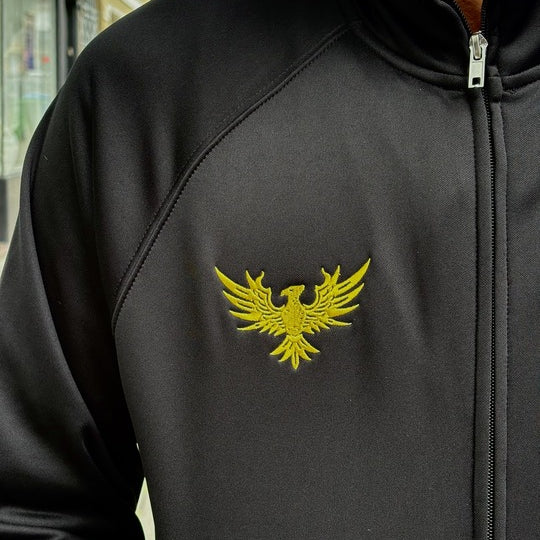 A person wearing the WC x SFP Zip-Up Jacket, featuring a yellow phoenix emblem on the chest.