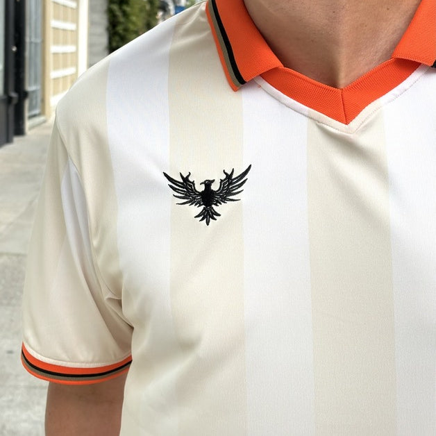 Person wearing the WC x SFP Jersey - Away, featuring a cream design, orange collar, and eagle emblem on the left chest.