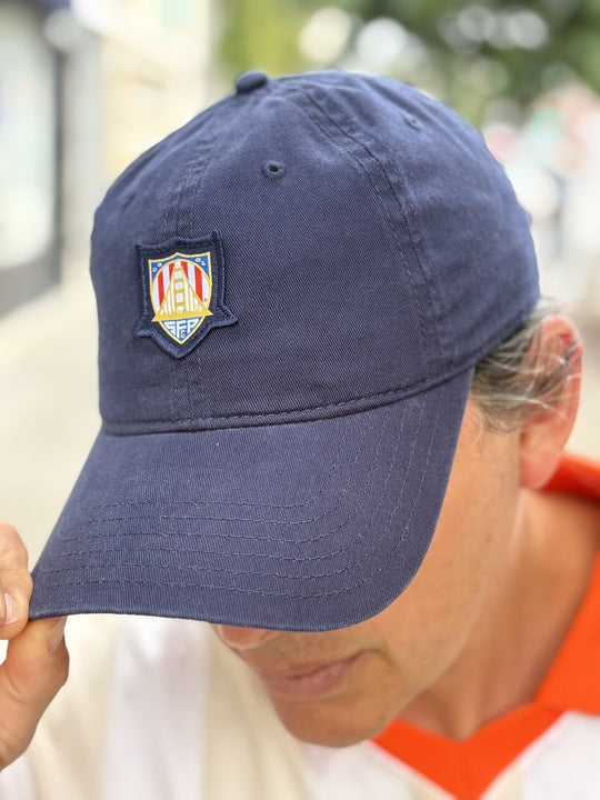 Wearing the WC x SFP Patched Hat with an embroidered crest, a person bows their head and touches the brim—subtly showing support for the US Men's National Team.
