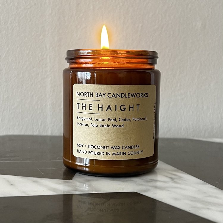 A lit brown jar candle from North Bay Candleworks sits gracefully on a marble surface, featuring The Haight label to capture the allure of the Bay Area.