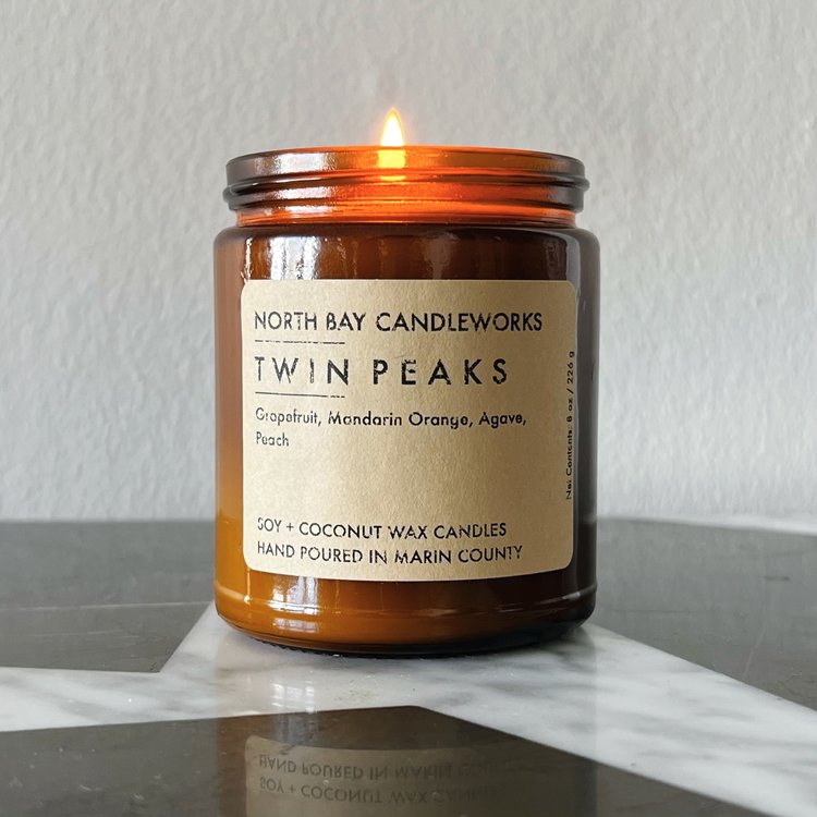 A candle from North Bay Candleworks, encased in a brown jar and labeled Twin Peaks, evokes the essence of the Bay Area with its invigorating blend of grapefruit, mandarin orange, agave, and peach scents.