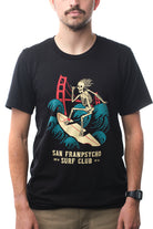 A man wears the ultra-soft and comfortable Surf Club Tee, featuring a skeleton surfing and the bold text "San Franpsycho Surf Club.