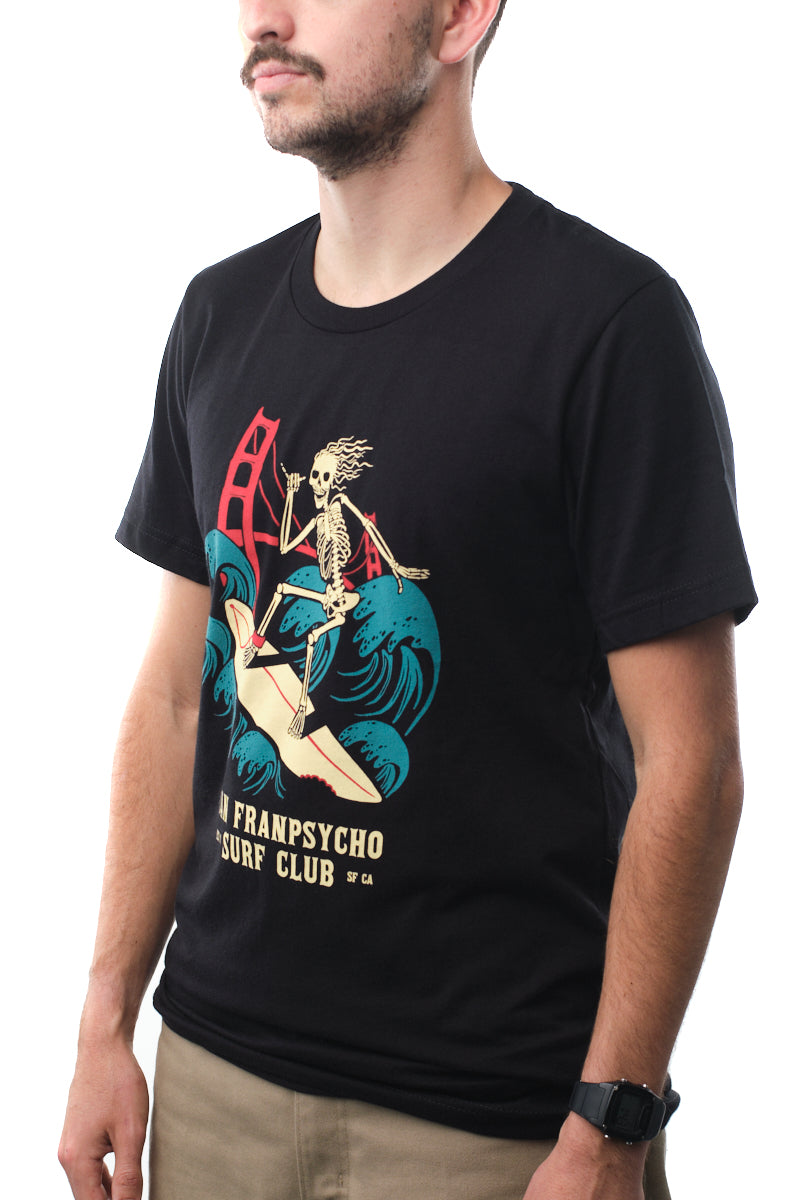 A man wearing a Super Soft Surf Club Tee in black, featuring a skeleton surf club graphic design.