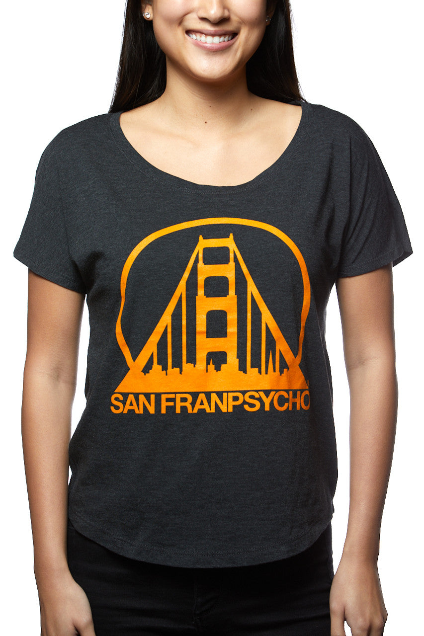 A smiling person dons the Charcoal & Orange Dolman, a scoop neck tee featuring a vibrant orange Golden Gate Bridge design and the iconic San Franpsycho text, all hand printed in San Francisco.