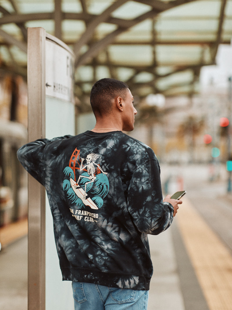 A person in the cozy Surf Club Crewneck sweatshirt stands at the station, clutching a phone.
