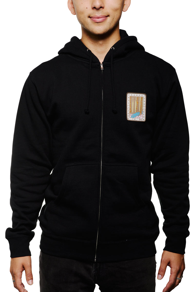 A person wearing the Black Muir Woods Patched Zip-Up Hoodie made from 100% cotton, featuring a small colorful patch on the chest, ideal for those who love to wander.