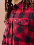 A person with dreadlocks is showcasing the chest pocket details of the super soft Red & Black Checkered SFP Flannel.
