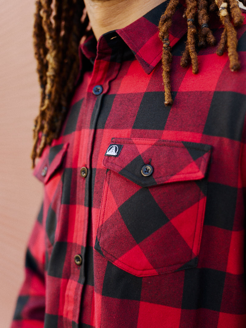 A person with dreadlocks is showcasing the chest pocket details of the super soft Red & Black Checkered SFP Flannel.
