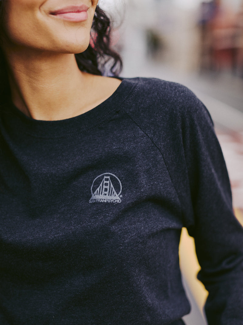A woman wearing the Charcoal Raglan w/ Mini Logo, part of our basics line, featuring a small logo of a bridge with San Francisco text. It's perfect for everyday wear with its effortless style and comfort.