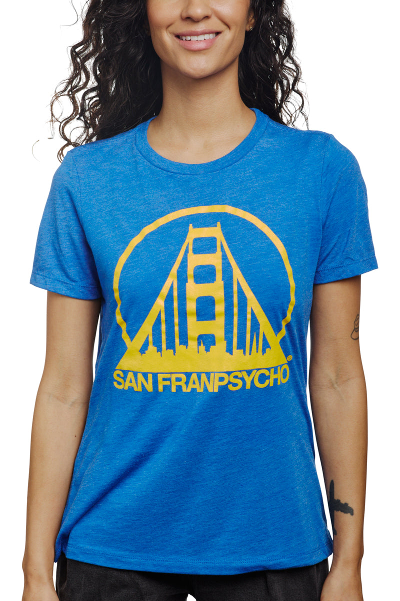 A smiling woman wearing the Women's Logo Tee - Blue & Gold, featuring a yellow bridge graphic and San Franpsycho text, crafted from a soft poly/cotton/rayon blend.